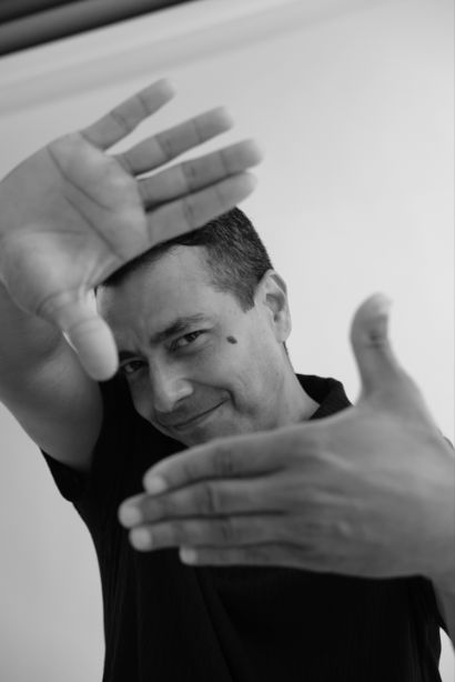 Daniel Garrido in black and white, making an 'ok' sign with his hand in front of his eye.
