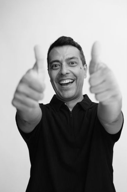Daniel Garrido in black and white, showing two thumbs up with an enthusiastic smile.