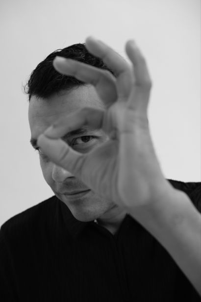 Daniel Garrido in black and white, making an 'ok' sign with his hand in front of his eye.